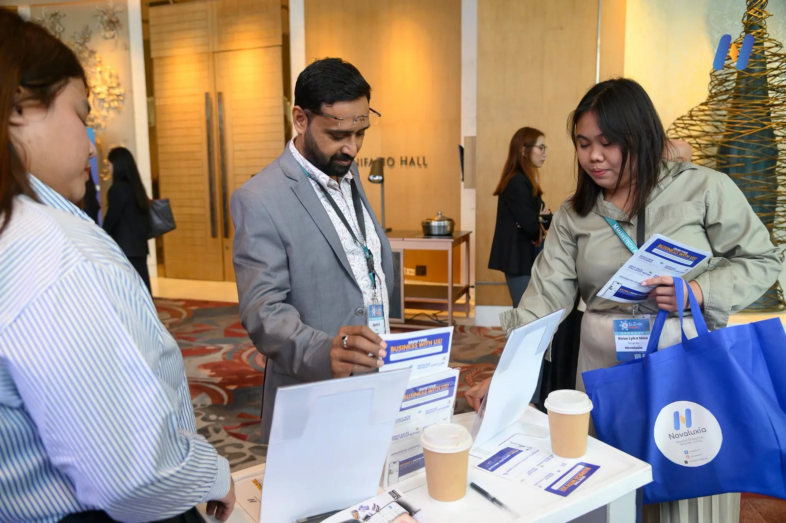 The Novaluxia side table at a summit venue, the app open on the table-top display and a blue tote bag beside it